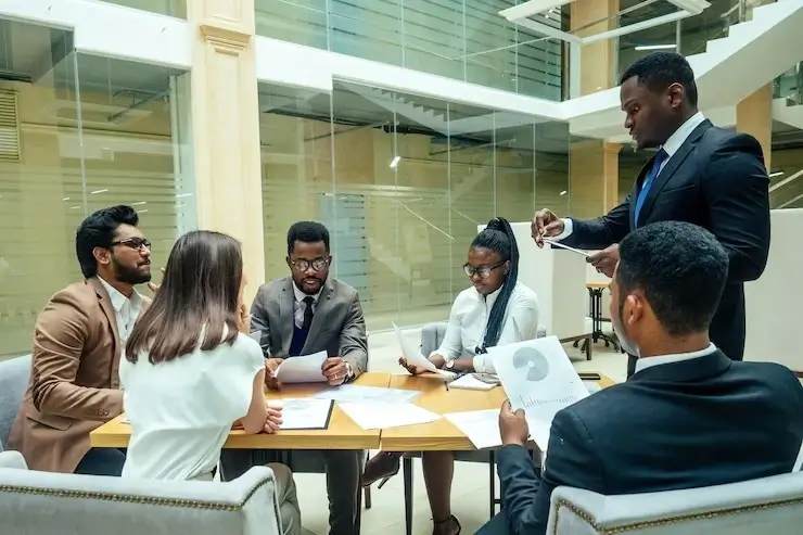 Group of workers engaged in a mentorship program, with one individual speaking and the rest listening attentively.