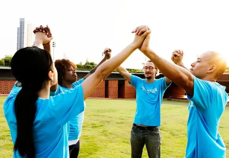 A group of diverse people with their hands raised and arms linked, looking up to the sky