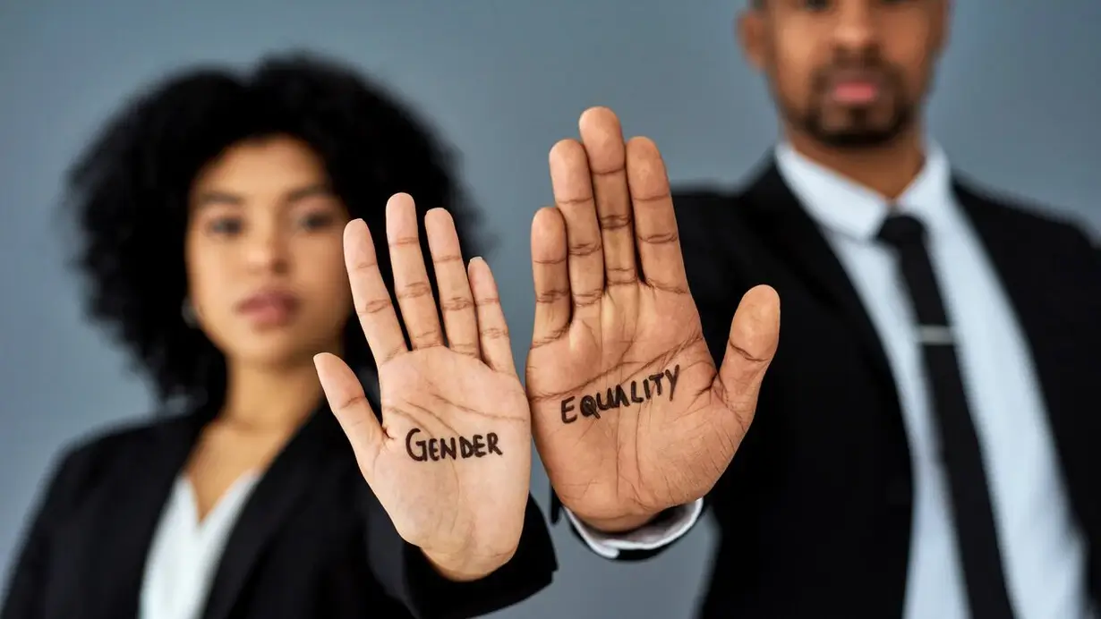 A woman and a man with their hands held up with the phrase 'gender equality' written in their palms.