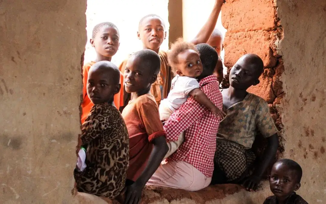 A group of children sitting in a window of an unfinished building, looking at the camera