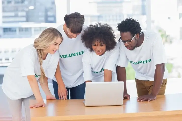 Group of happy volunteers smiling and looking at a laptop together