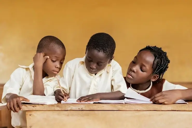 Three children in a classroom, doing schoolwork at their desk